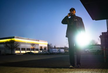 Security Guard Walking Building Perimeter With Flashlight At Night